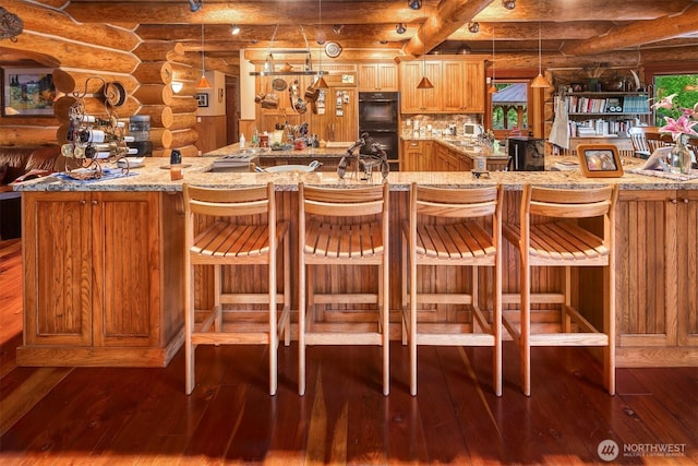 interior space with a kitchen breakfast bar, rustic walls, dobule oven black, and dark wood-type flooring