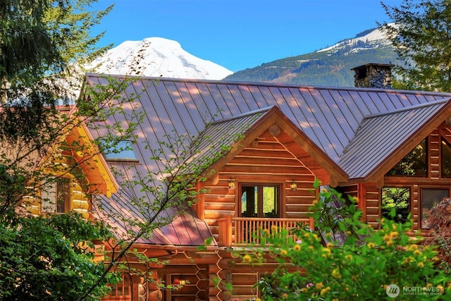 view of home's exterior with a standing seam roof, metal roof, a chimney, log siding, and a mountain view