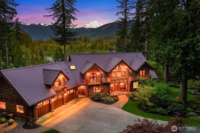 view of front of house featuring a balcony, a standing seam roof, metal roof, driveway, and a forest view