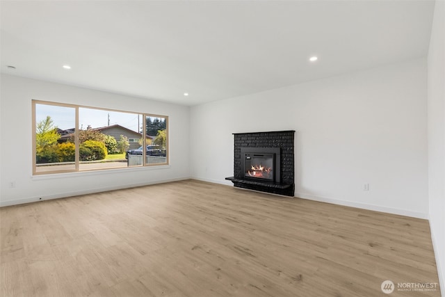 unfurnished living room with baseboards, a brick fireplace, and light wood finished floors