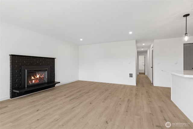 unfurnished living room with a brick fireplace, light wood-style flooring, recessed lighting, baseboards, and visible vents