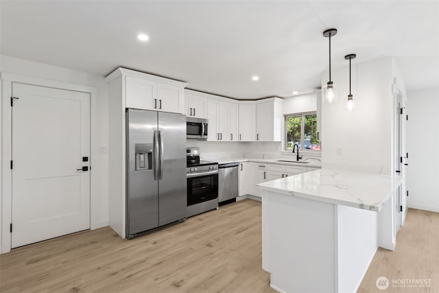 kitchen with a sink, appliances with stainless steel finishes, light wood-type flooring, and a peninsula