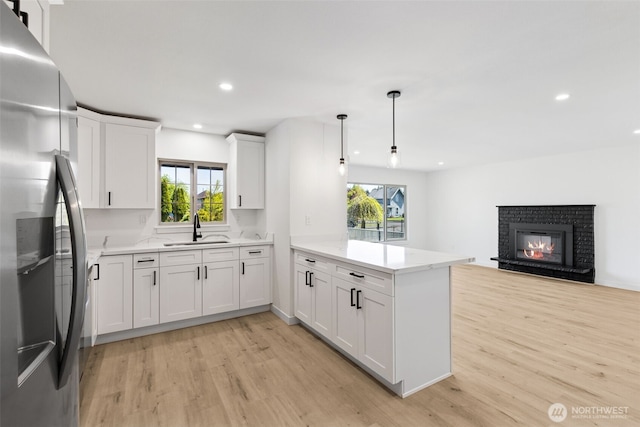 kitchen featuring a peninsula, a healthy amount of sunlight, stainless steel refrigerator with ice dispenser, light wood-type flooring, and a sink