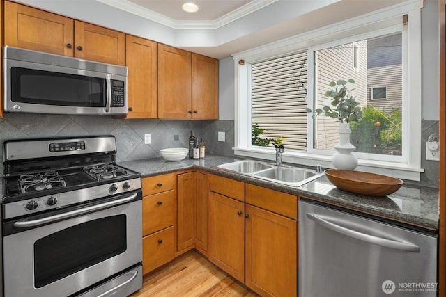 kitchen featuring brown cabinetry, ornamental molding, light wood-style floors, a sink, and appliances with stainless steel finishes