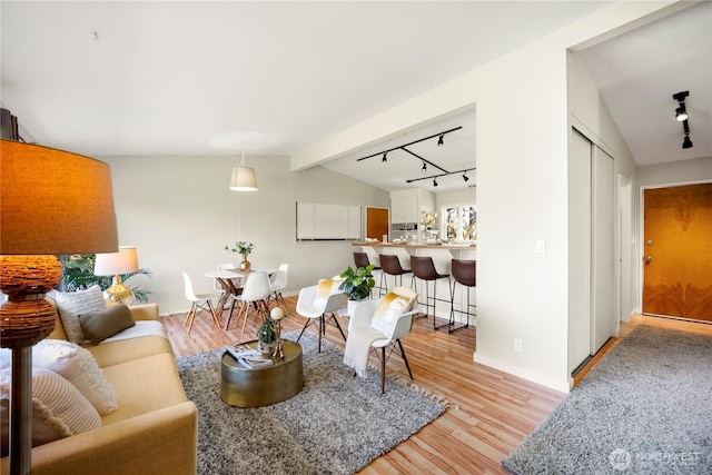 living room featuring light wood-type flooring, lofted ceiling with beams, and track lighting