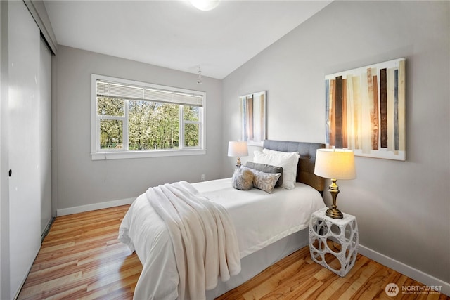 bedroom featuring baseboards, wood finished floors, vaulted ceiling, and a closet