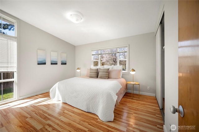 bedroom featuring light wood-type flooring, baseboards, lofted ceiling, and multiple windows