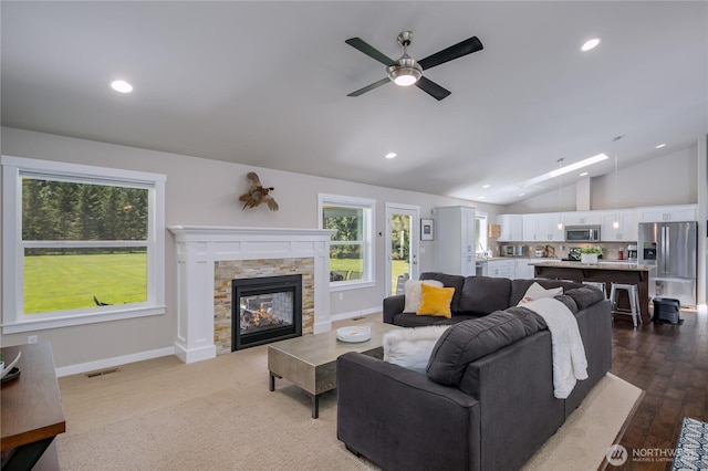 living room featuring a wealth of natural light, a ceiling fan, a stone fireplace, and lofted ceiling