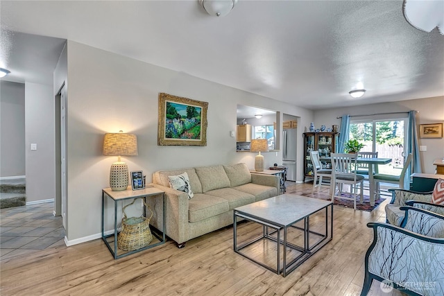 living room with a textured ceiling, baseboards, and light wood-type flooring
