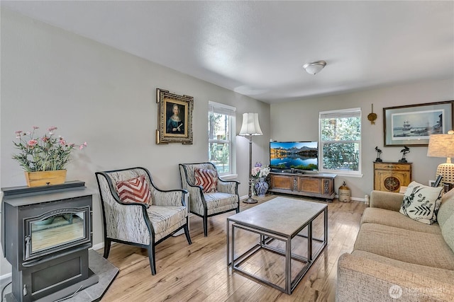 living room with a healthy amount of sunlight, baseboards, a wood stove, and wood finished floors