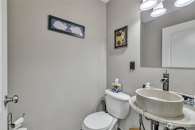 bathroom with a sink, a textured wall, and toilet