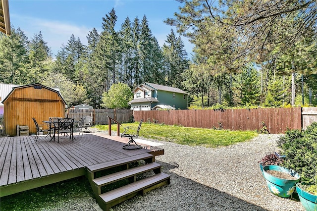 view of yard featuring outdoor dining space, a storage shed, a deck, a fenced backyard, and an outbuilding