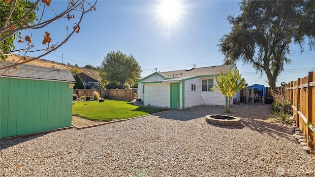 rear view of house with an outdoor structure, a fenced backyard, a storage unit, a yard, and a fire pit