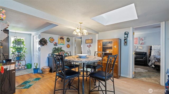 dining room featuring a textured ceiling, a skylight, an inviting chandelier, and light wood finished floors
