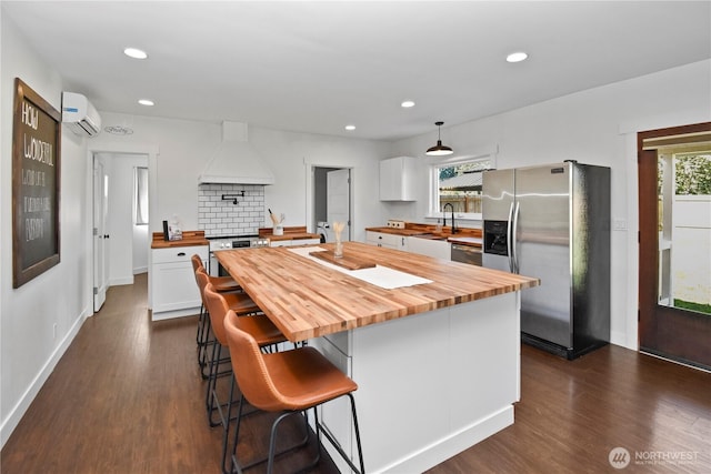 1517 Pioneer Hwy, Silvana, WA 98287 - kitchen with custom exhaust hood, an AC wall unit, white cabinetry, wood counters, and appliances with stainless steel finishes
