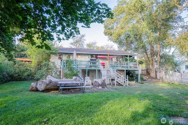 rear view of house with a lawn, fence, a wooden deck, and stairs