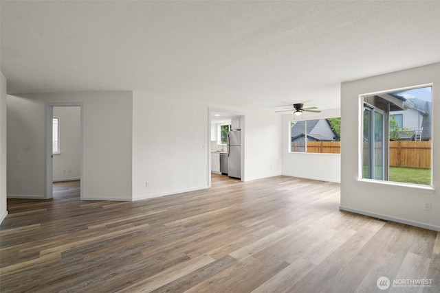 unfurnished living room featuring a healthy amount of sunlight, baseboards, ceiling fan, and wood finished floors