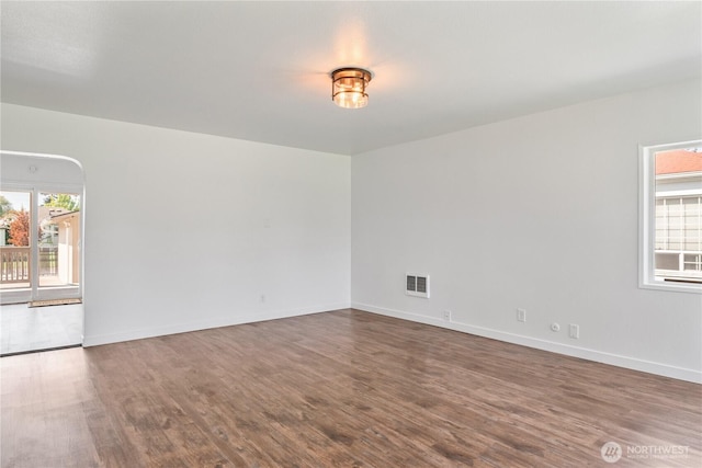 unfurnished room with baseboards, dark wood-style floors, and visible vents