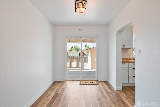 doorway featuring arched walkways, baseboards, and light wood-style floors