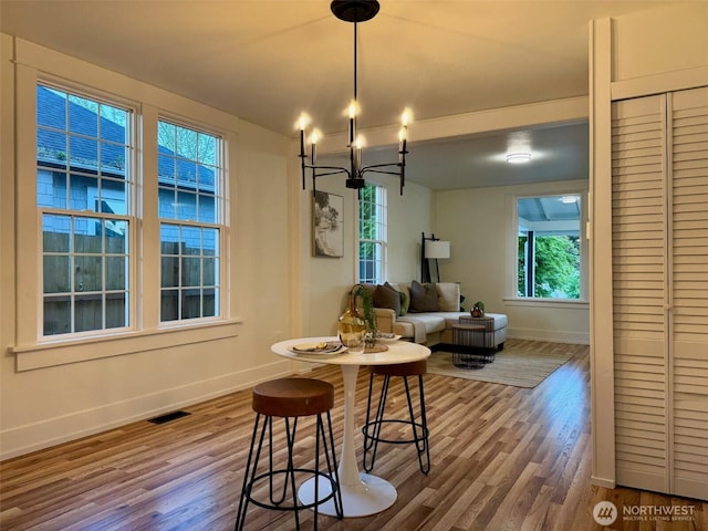 dining area featuring baseboards, visible vents, wood finished floors, and a notable chandelier