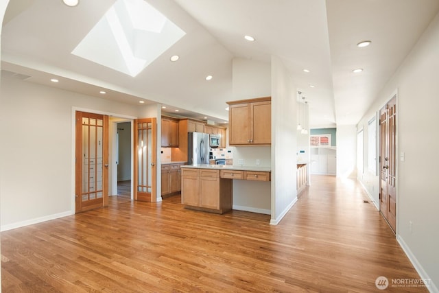 kitchen with appliances with stainless steel finishes, light countertops, light wood-style flooring, recessed lighting, and a skylight