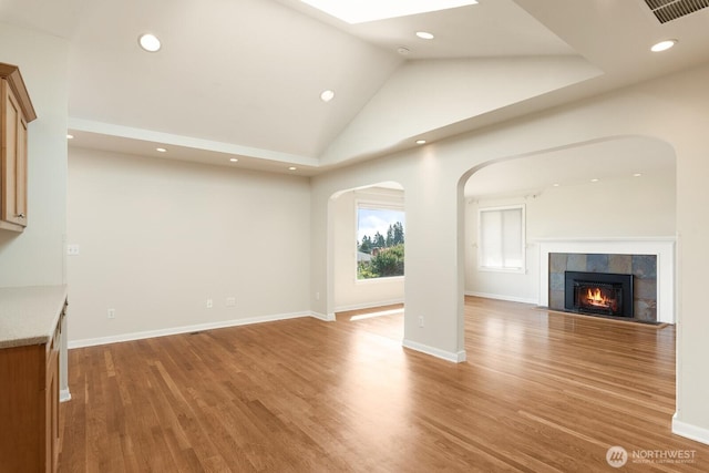 unfurnished living room featuring arched walkways, light wood finished floors, and vaulted ceiling with skylight