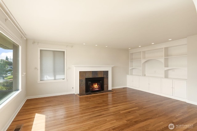 unfurnished living room with baseboards, visible vents, a tiled fireplace, and wood finished floors