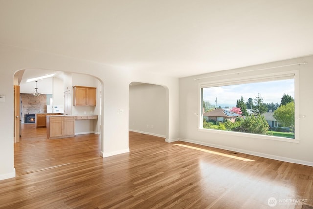 unfurnished living room featuring arched walkways, baseboards, and light wood-style floors