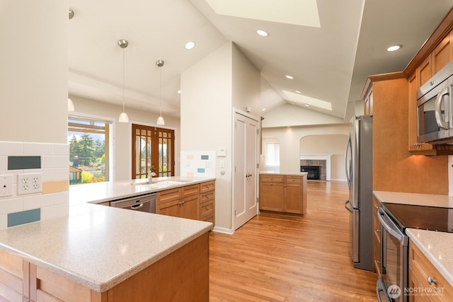 kitchen with a peninsula, vaulted ceiling with skylight, a sink, light wood finished floors, and stainless steel appliances