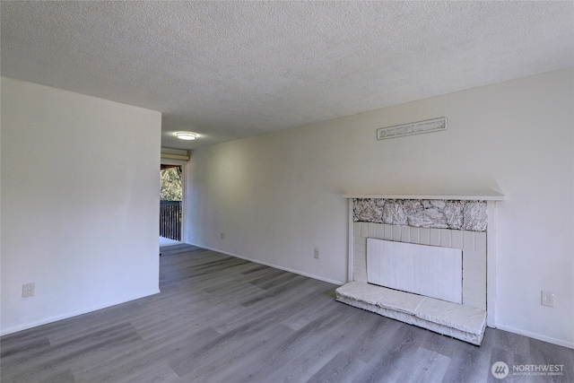 1917 E 60th St, Tacoma, WA 98404 - unfurnished living room featuring baseboards, a fireplace with raised hearth, a textured ceiling, and wood finished floors
