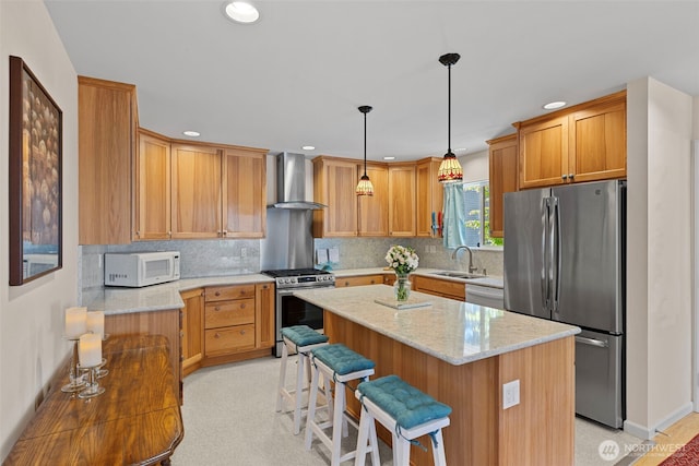 kitchen featuring stainless steel appliances, wall chimney range hood, a sink, a kitchen island, and light stone counters