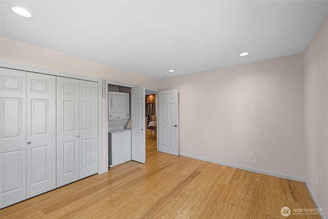 unfurnished bedroom with stacked washing machine and dryer, light wood-style flooring, baseboards, recessed lighting, and a closet