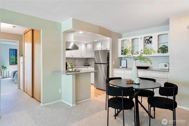 912 3rd Ave W Unit 303, Seattle, WA 98119 - kitchen with freestanding refrigerator, a peninsula, wall chimney exhaust hood, light carpet, and white cabinets