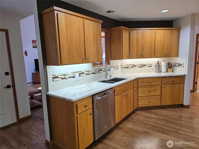 kitchen featuring stainless steel dishwasher, wood finished floors, light countertops, a sink, and backsplash