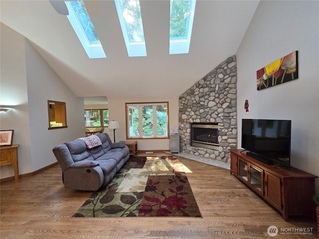 living area with high vaulted ceiling, a skylight, a stone fireplace, and wood finished floors