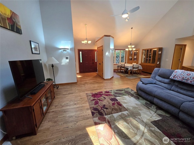 living room with high vaulted ceiling, baseboards, ceiling fan with notable chandelier, and light wood-type flooring