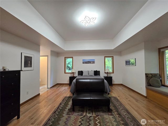 bedroom featuring a tray ceiling, baseboards, and light wood finished floors