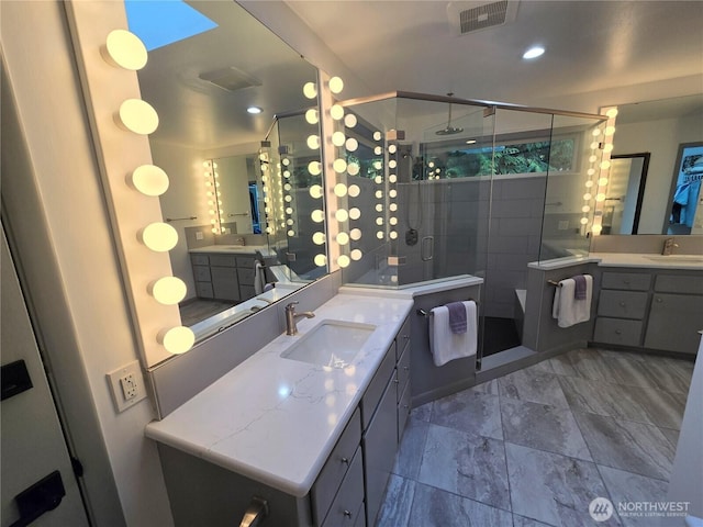 full bath with two vanities, visible vents, a shower stall, and a sink