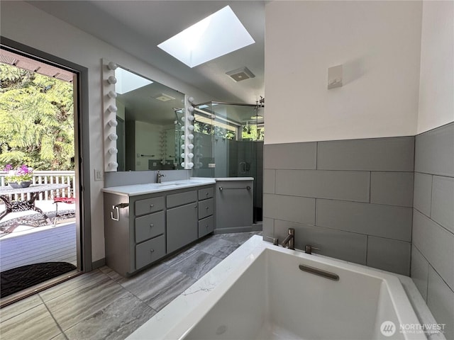 bathroom with vanity, a skylight, visible vents, a bath, and a stall shower