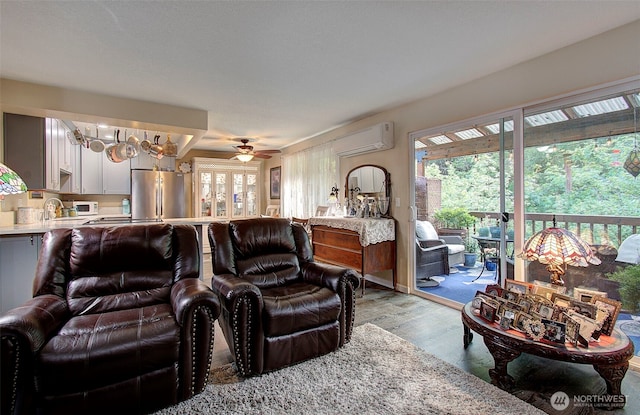 living room with a wall mounted air conditioner, light wood-style flooring, and ceiling fan