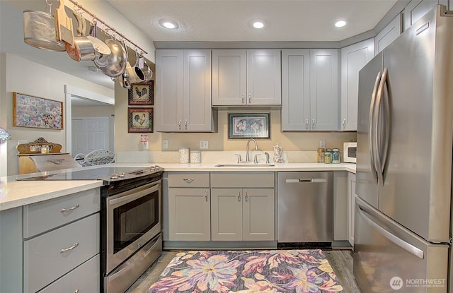 kitchen with a peninsula, recessed lighting, a sink, gray cabinetry, and stainless steel appliances