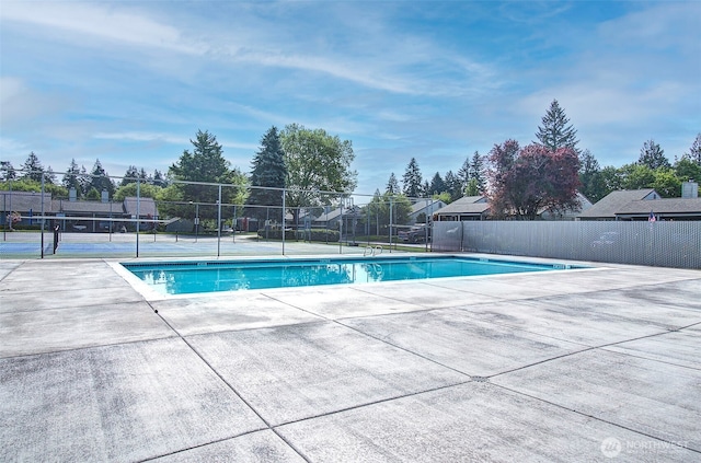 community pool with fence, a tennis court, and a patio area