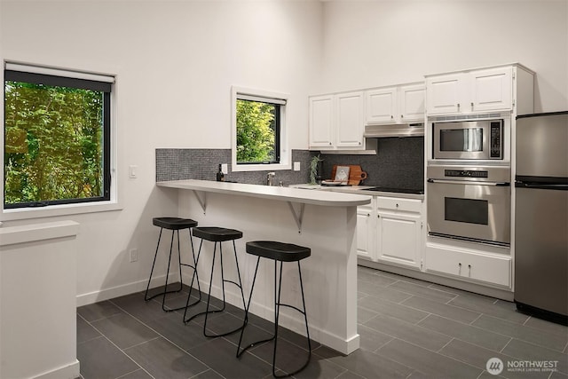 kitchen featuring under cabinet range hood, a kitchen bar, white cabinets, and appliances with stainless steel finishes