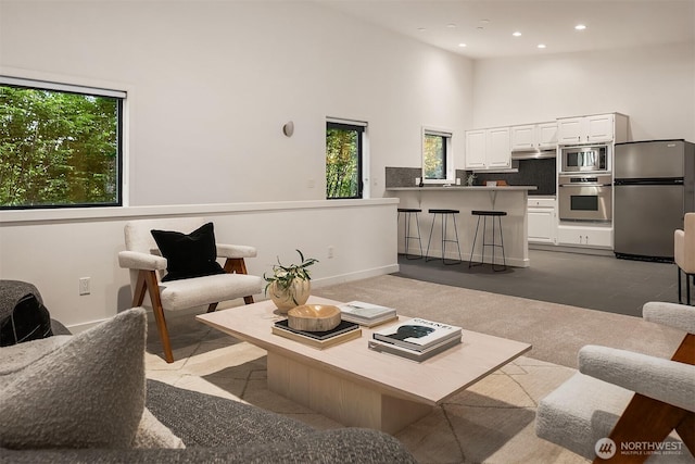 living area featuring plenty of natural light, dark colored carpet, a towering ceiling, and recessed lighting