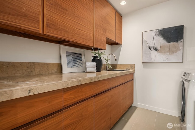 clothes washing area featuring a sink, washer / clothes dryer, cabinet space, light tile patterned flooring, and baseboards