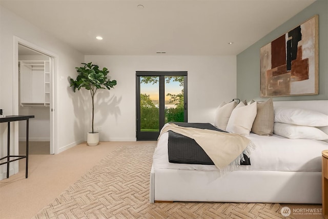 bedroom with a walk in closet, light colored carpet, baseboards, and recessed lighting