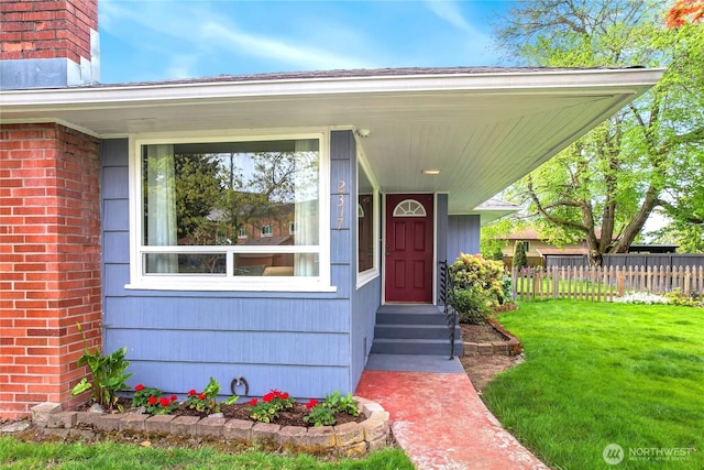 property entrance with a lawn, brick siding, fence, and a chimney