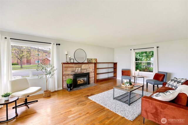 living room featuring baseboards, a stone fireplace, and light wood finished floors