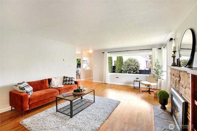 living area with baseboards, a stone fireplace, and light wood finished floors