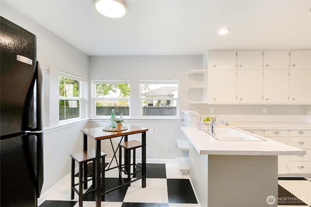 kitchen featuring a sink, light countertops, baseboards, freestanding refrigerator, and tile patterned floors